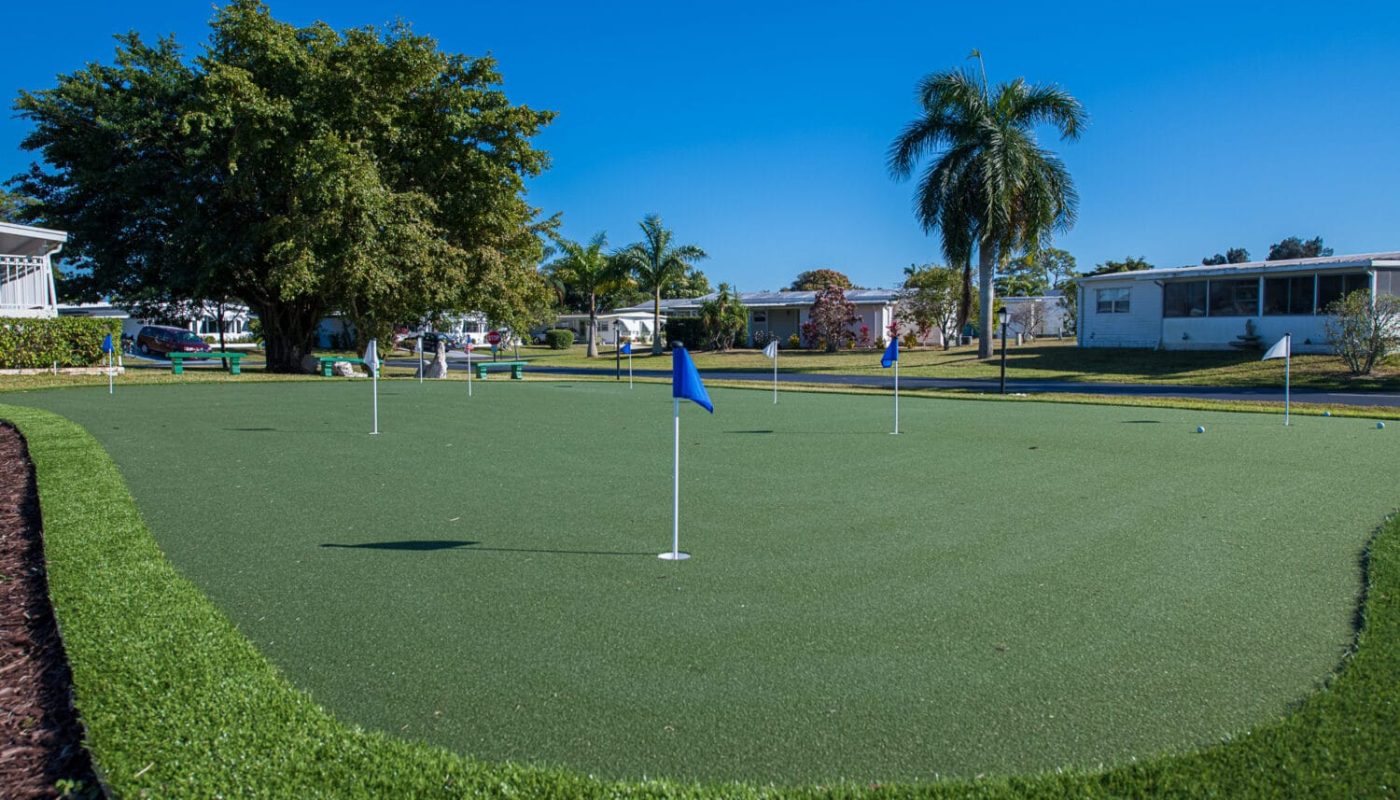 Mini golf putting green with flags and nearby homes under a sunny sky in boynton beach fl