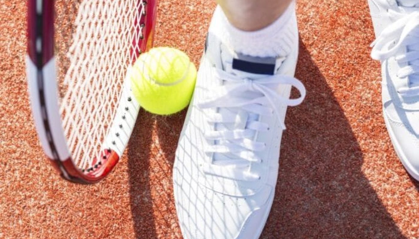 Close-up of a tennis racket, yellow ball, and white sneakers on a clay court in boynton beach fl